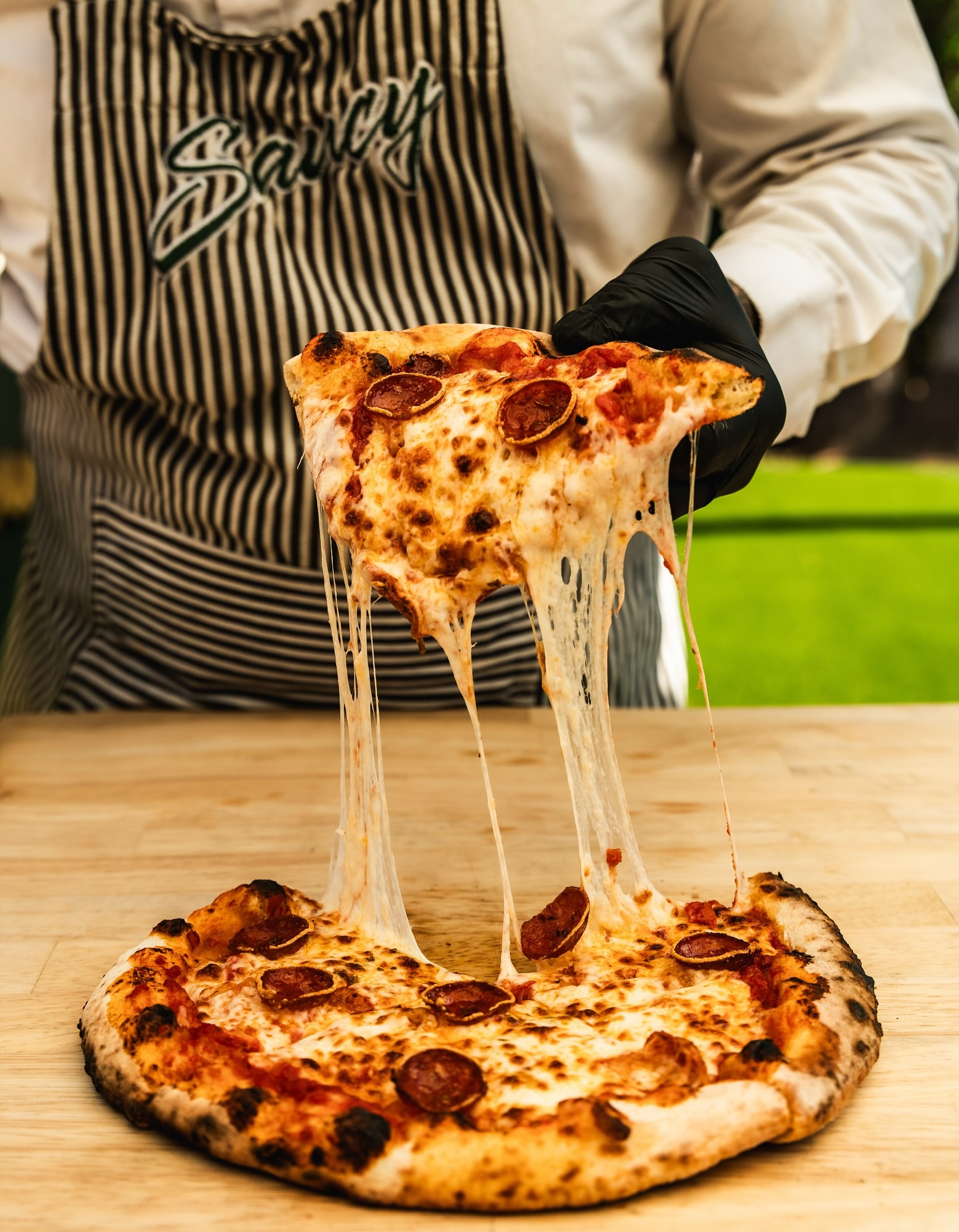 A freshly fired pepperoni pizza being pulled apart with stretchy melted cheese