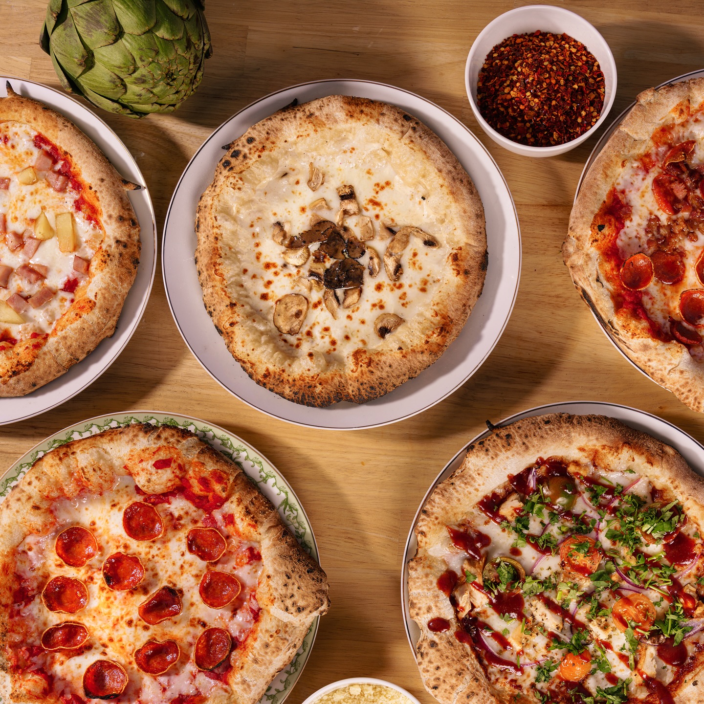 A tabletop spread of freshly fired Saucy pizzas